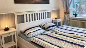 Un dormitorio con dos camas, una mesita de noche con lámpara, una ventana con cortinas y un cuadro en la pared.