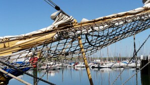 Primer plano de una red y cuerdas de barco, con un puerto deportivo y embarcaciones al fondo.