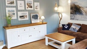 Una sala de estar con un aparador blanco, un sofá marrón, una mesa de centro de madera y una pared decorada con marcos.