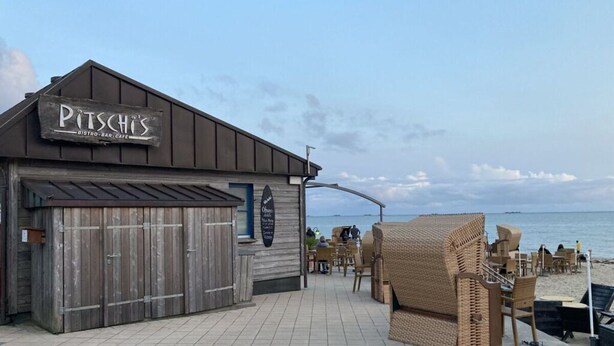Un restaurante frente al mar llamado "Pitschs" con fachada de madera rústica, mesas al aire libre y vistas al océano.