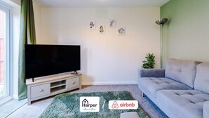 A living room with a flat-screen TV, a grey sofa, a green rug, and a wall with three framed pictures. - Cosy 3BR Deeside Sleeps 5 | Contractor Stays (Flintshire)
