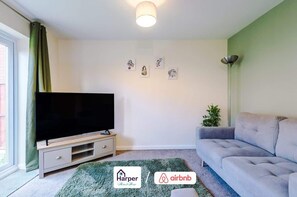 A living room with a flat-screen TV, a grey sofa, a green rug, and a wall with three framed pictures. - Cosy 3BR Deeside Sleeps 5 | Contractor Stays (Flintshire)