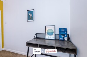 Une pièce avec un bureau en bois foncé, un tableau encadré représentant un zèbre, un tableau encadré représentant un bâtiment et une boîte contenant un sèche-cheveux.