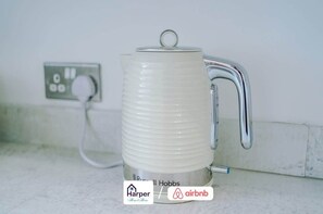 Una tetera eléctrica blanca con asa y cable de alimentación conectado a un enchufe.
