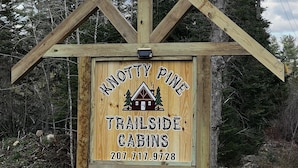 A wooden sign for Knotty Pine Trailside Cabins with a contact number.