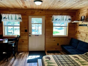 A cabin interior with a dining area, a sofa, and two windows with curtains.
