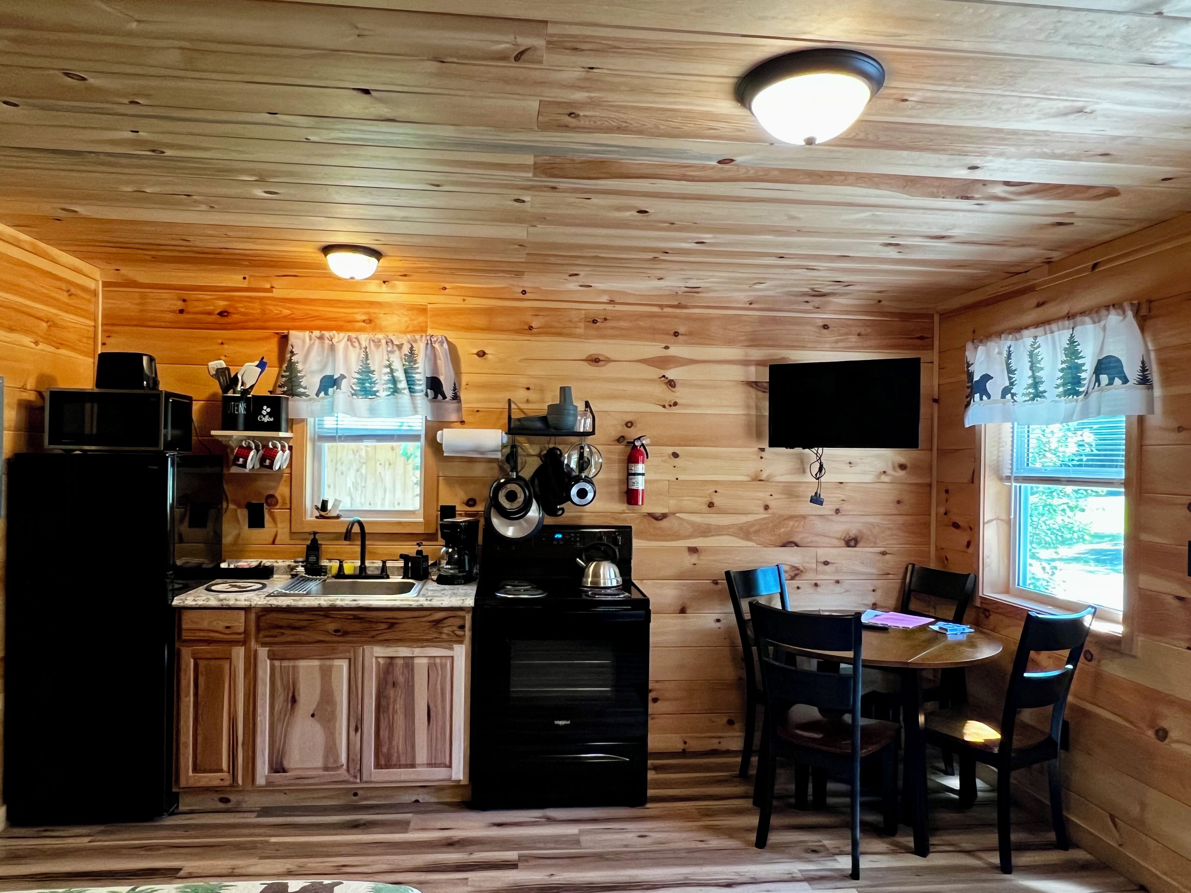 A wooden cabin interior with a kitchen, dining area, and a fireplace.