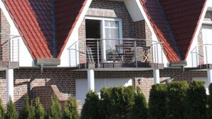 A modern building with a red-tiled roof, brick walls, and a balcony with railings. - Holiday Apartment Susewind (Borkum)