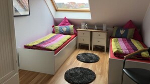 A small, cozy bedroom with a sloped ceiling and a skylight. It features two single beds with colorful bedding, a small desk with a chair, and a framed picture on the wall. - Holiday Apartment Susewind (Borkum)