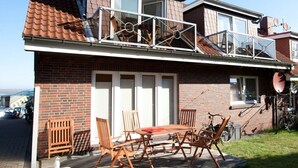 A two-story house with a balcony, brick exterior, and a patio with wooden furniture. - A in Haus Seewind Comfortable Vacation Home (Wittduen)
