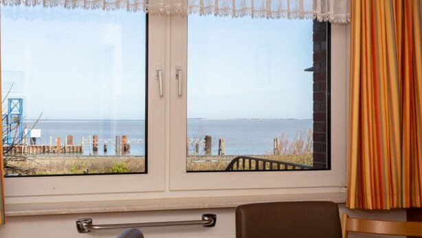 A room with two windows overlooking a beach, a chair, and a bed. - A in Haus Seewind Comfortable Vacation Home (Wittduen)