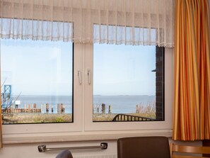 A room with two windows overlooking a beach, a chair, and a bed. - A in Haus Seewind Comfortable Vacation Home (Wittduen)
