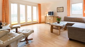 A spacious living room with a sofa, a table, and a TV on a wooden cabinet. - A in Haus Seewind Comfortable Vacation Home (Wittduen)