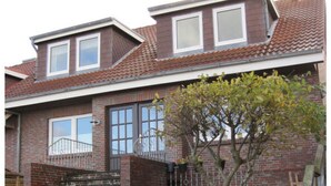 A two-story brick house with a small front yard, a tree, and a staircase leading to the entrance. - A in Haus Seewind Comfortable Vacation Home (Wittduen)