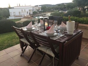 Une table à manger installée à l’extérieur, avec des chaises, une bougie et une bouteille de champagne.
