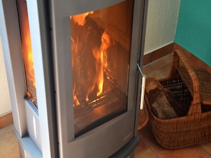 A wood-burning stove with visible flames, a wicker basket, and a tiled floor. - Charmante Ferienwohnung Vincent in Strandnaehe (Insel Poel)