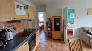 Une cuisine compacte équipée d’une cuisinière, d’un évier et de placards, qui donne sur une chambre avec un lit et une vue sur l’extérieur.