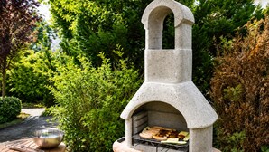 Un barbecue extérieur en pierre, doté d’une cheminée, entouré de verdure.