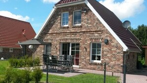 A brick house with a sloped roof, a satellite dish, and a patio with outdoor furniture. - House Little Maddi Comfortable Vacation Home (Dornum)