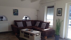 A living room with a brown sofa, a coffee table, a radiator, and a window with blinds. - House Little Maddi Comfortable Vacation Home (Dornum)