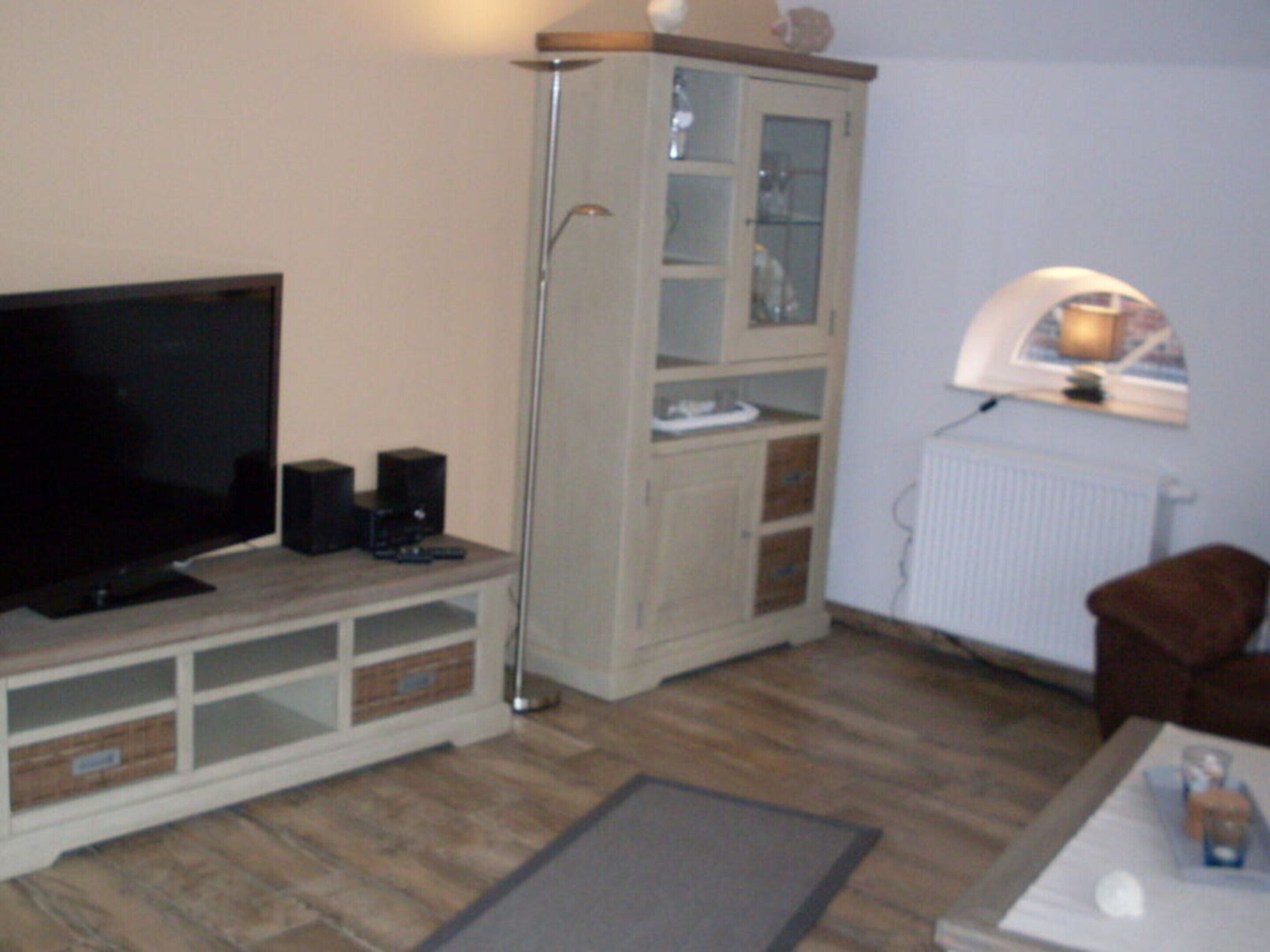 Un salon équipé d’un téléviseur à écran plat, d’enceintes, d’un meuble, d’un radiateur et d’un fauteuil marron.