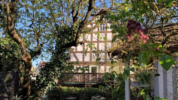A courtyard with a table and chairs, surrounded by greenery and a building with a balcony. - Werts HOF Holiday Home (Rauschenberg)