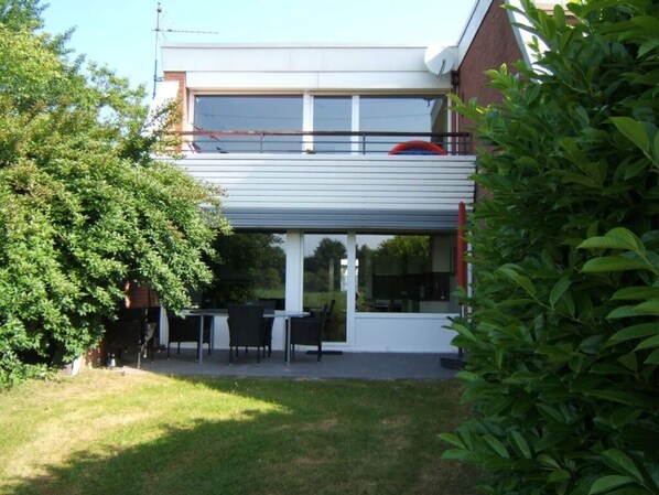 A modern two-story house with a covered patio area featuring outdoor furniture.