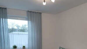 Una camera da letto con un letto, tende, una finestra con piante e una lampada a soffitto.