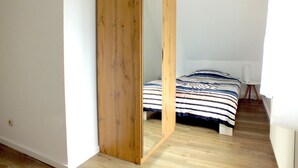 A bedroom with a bed, a wooden wardrobe, and a small white table. - Holiday Home in Lichtenau With Garden Bliss (Lichtenau)