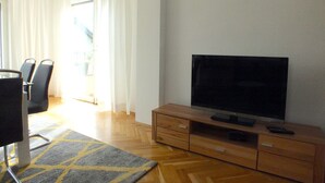 A living room with a flat-screen TV on a wooden cabinet, a dining area with chairs, and a patterned rug on the floor. - Holiday Home in Lichtenau With Garden Bliss (Lichtenau)