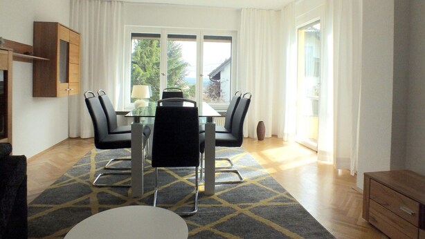 A modern dining area with a glass table, black chairs, and a view of trees through large windows. - Holiday Home in Lichtenau With Garden Bliss (Lichtenau)