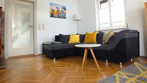 A living room with a dark grey sectional sofa, a small round table, and a painting on the wall. - Holiday Home in Lichtenau With Garden Bliss (Lichtenau)