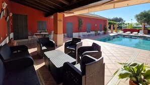 An outdoor pool area with wicker furniture and a red building in the background. - Belvilla by OYO Villa Valencina de la Concepcion (Valencina de la Concepcion)