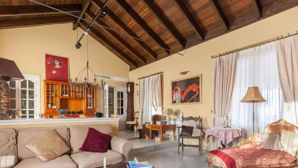 A spacious living room with a high ceiling, a sofa, a coffee table, a dining area, and a kitchen visible through an open door. - Belvilla by OYO Villa Valencina de la Concepcion (Valencina de la Concepcion)
