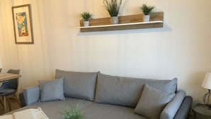 Ett modernt vardagsrum med en grå soffa, ett litet runt bord med en växt och en trähylla med krukväxter.