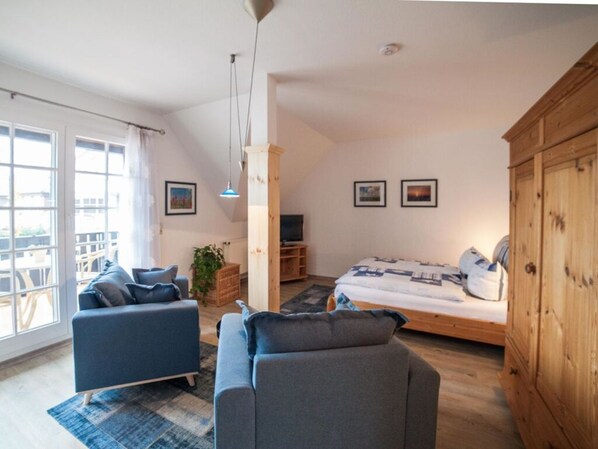 A modern living room with a sofa, a bed, and a wooden cabinet. - Holiday Apartment Lutt Matten (Zingst)