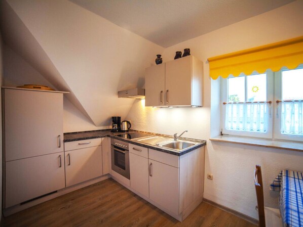 Uma cozinha compacta com armários brancos, forno embutido e pia. Há uma janela com cortina amarela e vista para o exterior.