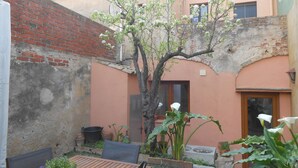 A courtyard with a brick wall, a wooden table, chairs, potted plants, and a tree with white flowers. - Villa a Palafrugell con Spiaggia di Mare (Palafrugell)