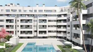 A modern multi-story hotel with a central swimming pool surrounded by lounge chairs and umbrellas, and a palm tree on the right. - Belvilla by OYO Apartamento Port Avenue (Marbella)