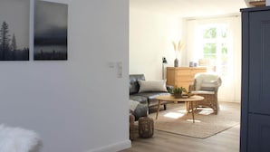 Una sala de estar moderna con un sofá, una mesa de centro y objetos decorativos. Se ve una escalera que sube a un nivel superior.