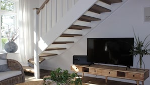 Una sala moderna con una escalera de madera, un televisor de pantalla plana sobre un mueble de madera, muebles de mimbre y una planta grande.