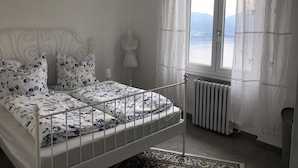 A bedroom with a bed, a window with curtains, a radiator, and a mannequin. - Majestic Apartment in Trarego-viggiona (Trarego Viggiona)