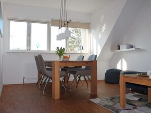 A modern dining area with a wooden table and chairs, a vase with flowers, and a view of the outdoors through large windows. - Holiday Apartment Priwall (Lübeck)