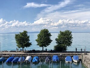 Eine Uferpromenade mit überdachten Booten, einer Steinpier und Bäumen entlang des Wasserufers.
