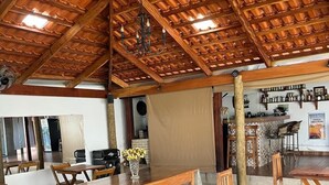 A spacious dining area with wooden tables and chairs, a high wooden ceiling, and a bar area in the background. - Pousada Sempre Viva  (São João Batista do Glória)