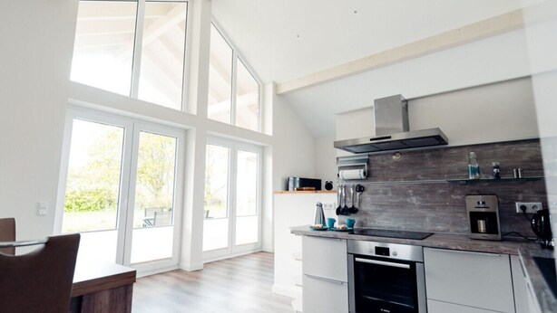 A modern kitchen with large windows, a built-in oven, and a stainless steel range hood. - Loheide Modern Retreat (Langenhorn)