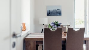 A dining area with a wooden table, two chairs, a vase with flowers, a lamp, and a framed picture on the wall. - Loheide Modern Retreat (Langenhorn)