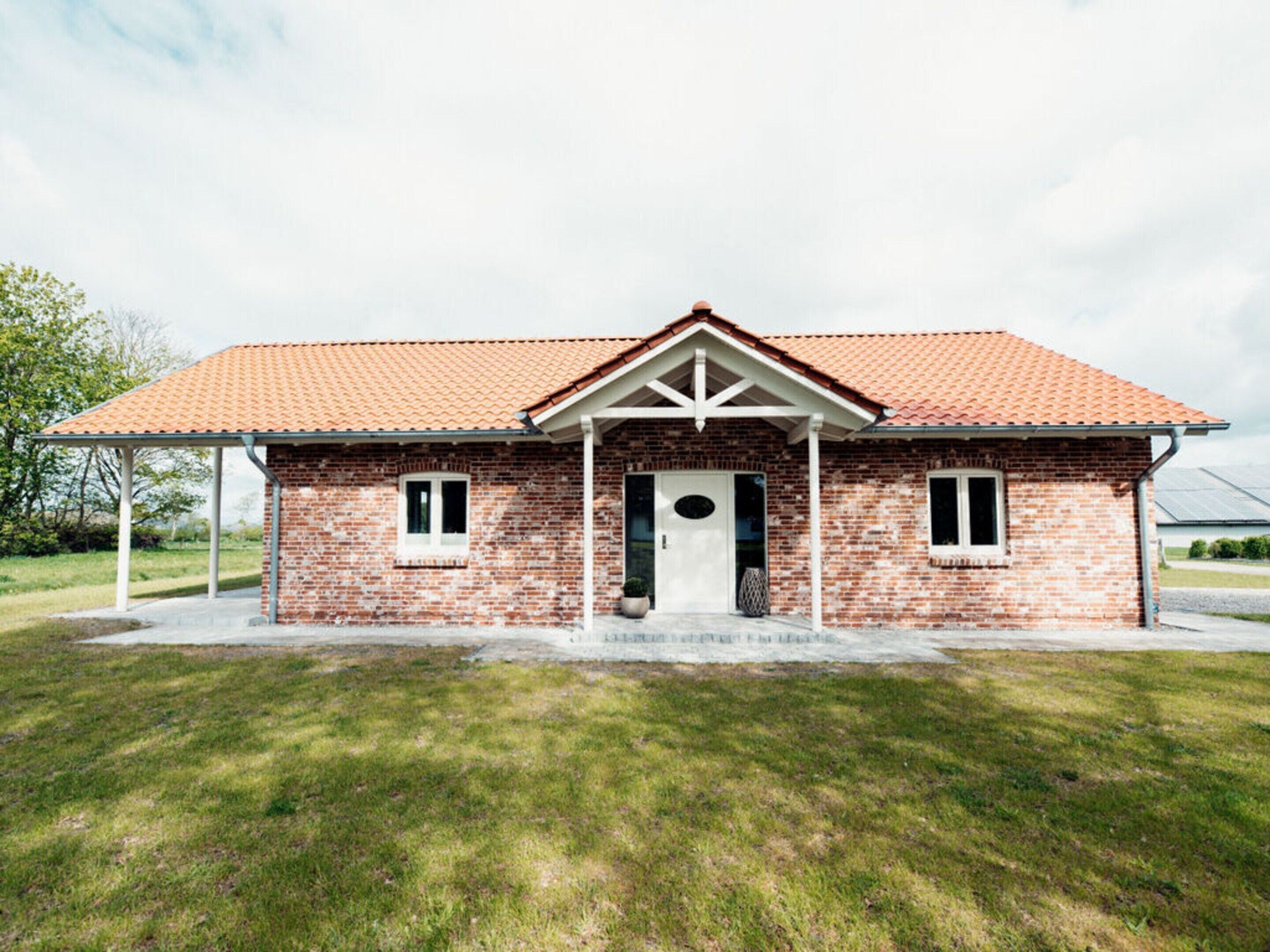 A single-story brick house with a red-tiled roof, a front porch, and a small front yard.