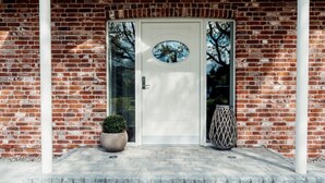 A brick building with a white door and a small potted plant in front. - Loheide Modern Retreat (Langenhorn)