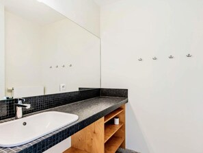 A bathroom with a white sink, black tiled countertop, and a large mirror. There are hooks on the wall and a wooden shelf below the countertop. - Les Mouettes 301 With Garage Located on the Dike (Koksijde)